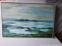 Full view of large horizontal canvas painting in silver wood frame showing an abstract landscape or seascape in blue, green and yellow colors with visible brush textures.