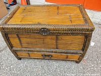 Front view of bamboo wicker trunk showing closed hinged lid with metal clasp and bottom drawer with metal handle.