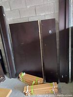 Photo of large dark brown wood panels and bundled wooden slats on floor in storage