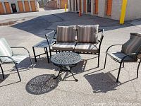 Full view of patio furniture set showing loveseat with two cushions, two armchairs with cushions, two side tables, and one round coffee table.