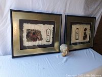 Lot displaying two framed Egyptian papyrus artworks and the carved statue of an Egyptian woman's head on a table with a plain white sheet.