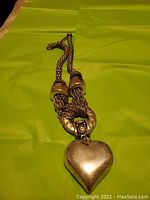 Full view of silver-toned chunky necklace laid flat on green background, showing heavy woven chain and large heart pendant.