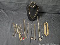 Photo showing 11 gold toned necklaces and bracelets, various chain styles and stones including red and black stones on pendants.