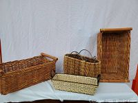 Overall view of four wicker baskets showing size differences and handle details on white cloth background