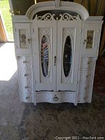 Front view of entire carved white-painted wooden bathroom cabinet showing mirrored center doors, side drawers and crown