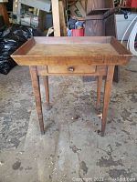 Front view of the wooden table showing tray top, drawer with knob, and four tapered legs.