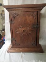 Front view of the wooden medicine cabinet showing the carved door with decorative corners and latch.