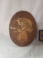 Oval wood plaque with etched image of girl with umbrella against textured background