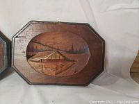 Wooden wall plaque with octagonal shape and painted image of a rural cabin near trees
