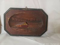 Photo showing a wooden wall plaque with a carved cabin and natural landscape, oval inset with frame, part of Quebec-themed set