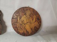 Round pyrography plaque showing seated man with a pipe.
