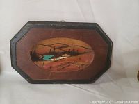 Wooden wall plaque with a rural scene featuring fields and a building, octagonal shape with black border