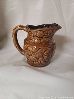 Photo of Bennington style cream pitcher with textured floral and leaf design and handle