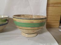 Side view of a ceramic bowl with wide green and yellow band and thin black and red stripes.