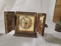Clock with enamel face and two side doors open revealing clock face with children playing image
