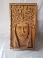 Front view of relief carved wooden panel depicting Native American chief with feather headdress and signature.