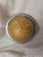 Yellowed vintage desk globe with metal base, showing continents and countries, mounted on a metal ring with degree markings.