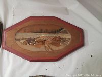 Wooden plaque with red border featuring a snowy log cabin in a winter landscape.