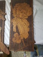 Wooden panel with pyrography image of a woman holding a rake, floral motif at bottom, signed and dated 1910