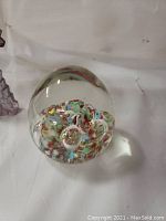 Colorful glass paperweight with bubbles and swirls inside a clear glass dome shape.
