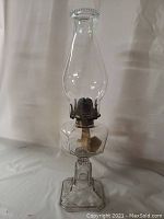 Complete clear glass oil lamp with metal burner assembly and glass chimney, standing upright against a plain background.