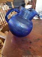 Blue ribbed glass water pitcher with round body and curved handle.