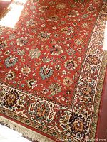 Full view of the 6x9 reddish floral patterned rug with cream intricate border and fringed edges, spread out on wooden flooring with sunlight exposure.