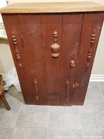 Front view of the wooden cupboard showing the two doors with decorative turned spindles and knobs, worn finish visible.