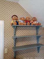Wide view of all five Berenstain Bears plush stuffed animals lined up on blue shelving against a wall with patterned wallpaper.