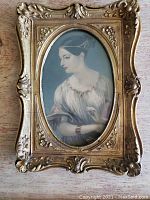 Front view of a hand-tinted miniature portrait of a woman in an ornate gilded frame. The portrait is oval-shaped inside a rectangular frame.