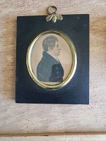 Front view of a miniature painted portrait of a man in profile set within a black frame with oval brass bezel and bee decoration