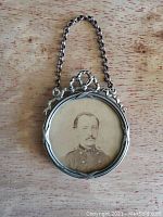 Front view of round pendant frame showing sepia vintage photo and silver-tone metal with decorative top and chain handle.