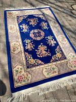 Full view of the rectangular vintage oriental carpet with blue center and floral border on a paved surface.