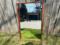 Full front view of rectangular mirror leaning against wooden fence, showing overall design and proportional dimensions