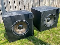 Pair of black JBL PSW-D110 subwoofer speakers with large front woofers and volume control knob on top right corner of each.