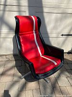 Full three-quarter front view of red vinyl swivel chair with white racing stripe, black shell frame, and aluminum base