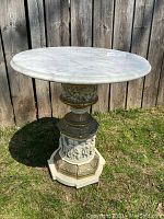 Full view of vintage side table with white Carrera marble top, visible veining, and decorative sculpted base on grass outdoors.