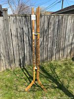 Full view of the vintage hockey stick coat tree outdoors against a wooden fence on grass.