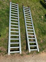 Two galvanized steel ramps laid side by side on grass, full overview of both.
