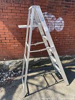 Full side view of the aluminum step ladder showing the open A-frame design, 5 steps, and platform tray on top, against a brick wall.