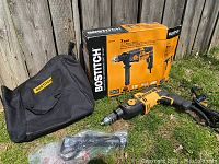 Full kit including drill, auxiliary handle, carrying bag and box placed on grass.