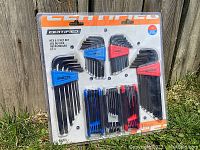 Photo of sealed Certified Hex Key Sets in original packaging showing blue and red color-coded holders with hex keys inside, against a wooden fence background.