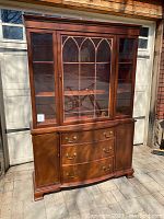 Front view of vintage china cabinet showing glass doors with decorative wooden trim, drawers and cabinet doors below.