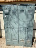 Front view of four light greenish-blue painted steel locker doors with vents and recessed handle indents