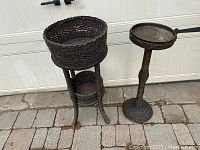 Front view of two antique wicker on wood painted planter stands on stone paver ground in front of white garage door.