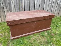 Rectangular brown painted wooden toolbox outdoors, showing top and one long side with paint wear and scratches