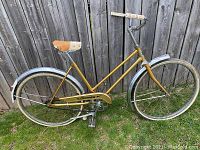 Full side profile of the vintage yellow Sears Fleetwing bicycle showing frame, fenders, seat, tires and chain guard.