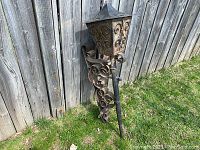 Full view of large wrought iron sconce light fixture standing upright outdoors, showing overall size and decorative scrollwork on the mounting bracket.