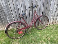 Side view of the complete vintage 1940's Toronto bicycle showing red steel frame, worn leather saddle, rear rack, license plate, and fenders.