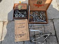 Lot photo showing two wooden boxes containing various tap and die tools and the Commercial Standards booklet on the ground.